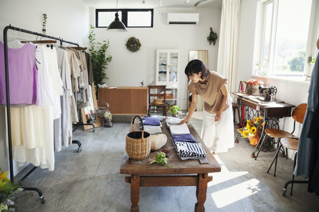 Japanese woman standing in a small fashion boutique, looking at T-Shirts on a coffee table.